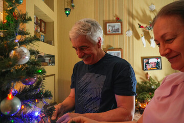Couple shares joyful moments indoors as they decorate a Christmas tree with colorful ornaments and lights