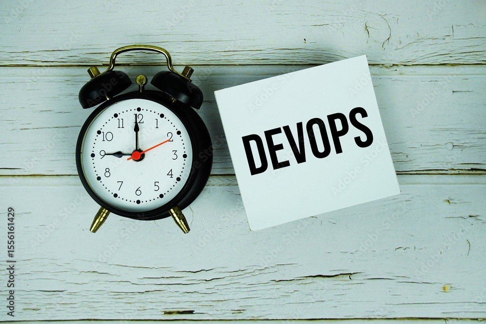 Poster devops text message on paper with alarm clock on wooden background