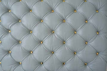 Close up of a light blue tufted leather surface with gold decorative studs