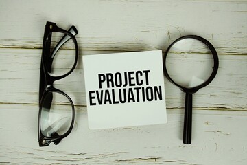 Project Evaluation text message on paper with magnifying glass and eyeglasses on wooden background