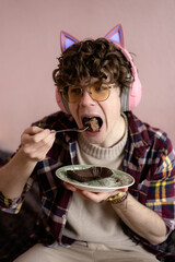 Enthusiastic young man enjoying a delicious dessert while wearing playful headphones in a cozy...