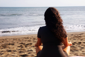 Woman meditating on sandy beach by sea, back view. Space for text