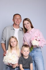 Family portrait of happy parents and their children with flowers on grey background