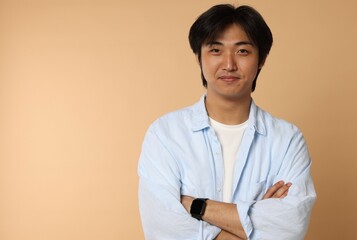 Portrait of handsome Asian man with crossed arms on beige background. Space for text