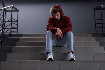 Bullying. Upset teenage boy on stairs indoors