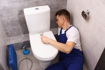 Professional plumber fixing toilet bowl in restroom
