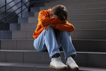Bullying. Upset teenage girl on stairs indoors