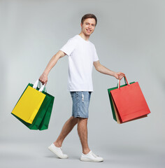 Cheerful man with shopping bags on light grey background