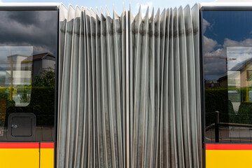Closeup on bus bellows of a yellow red bus. Reflection of a summer day in the city in the bus...