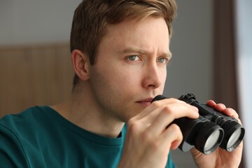 Paranoia. Worried man with binoculars at home