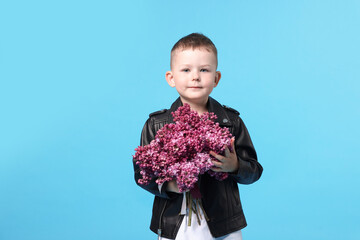 Little boy with bouquet of lilac flowers on light blue background