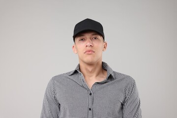 Young man wearing stylish black baseball hat on light grey background