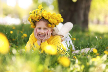 Cute little girl wearing wreath of dandelions on green grass in park