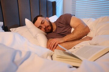 Young man sleeping with book in bed at home