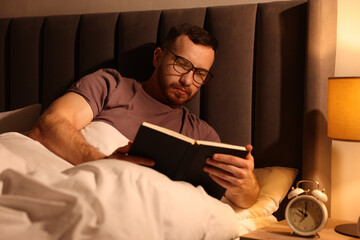 Young man reading book in bed at home
