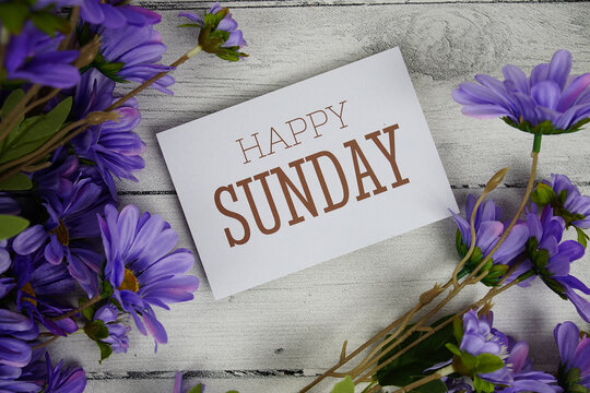 Happy Sunday text with flowers decoration on wooden background