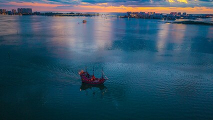 A lone pirate ship returns to port after a beautiful Florida sunset.  The lighted Sand Key bridge is shown in the background.