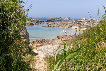 A beach with a rocky shoreline and a small path leading to the water. The water is calm and blue