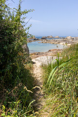 A beach with a rocky shoreline and a small path leading to the water. The water is calm and blue