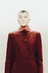 Woman with colorful short hair wearing a red coat stands confidently against a white background,...
