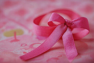 A vibrant pink satin ribbon tied into a bow with flowing tails against a textured fabric background with a floral pattern