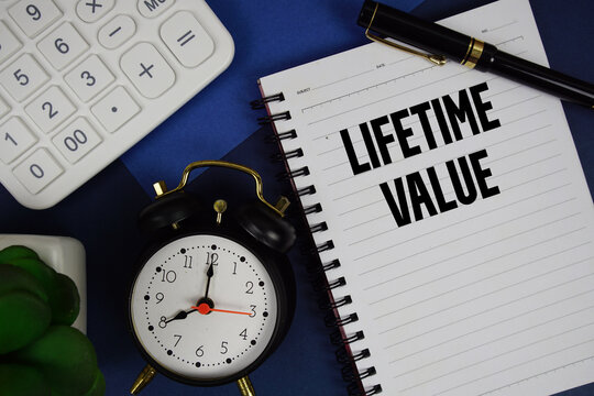Lifetime Value text written on notepad with calculator and alarm clock on navy blue background