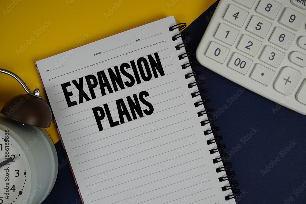 Poster expansion plans text written on notepad with calculator and alarm clock on navy blue background