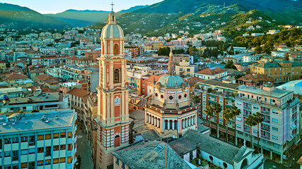High drone shot of basilica bell tower and ornate dome rising above Rapallo old town roofs against...