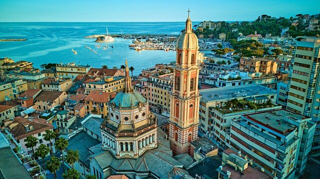 Aerial panorama of Rapallo basilica bell tower framed by yacht-filled harbor and Ligurian Sea, Italian Riviera coast, Italy. Drone view