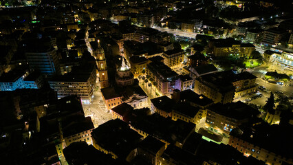 Vertical night aerial of Rapallo basilica campanile rising above glowing old-town streets on the Ligurian coast, Italian Riviera, Italy. Night drone view