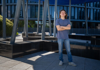 Full body portrait of confident young man with curly hair standing arms crossed in urban setting. Modern lifestyle, casual fashion, outdoor city concept.