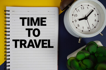 Time To Travel text written on notepad with alarm clock on blue background