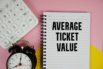 Average Ticket Value text written on notepad with calculator and alarm clock on pink background