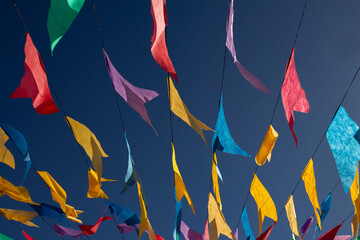 Close up em bandeirolas coloridas balan&ccedil;ando, penduradas em barbante, com c&eacute;u azul ao fundo.