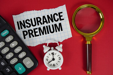 Insurance Premium text with alarm clock, magnifying glass anc calculator on red background