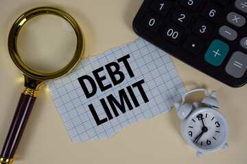 Debt Limit text with alarm clock, magnifying glass anc calculator on yellow background