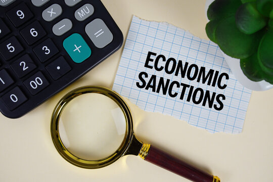 Economic Sanctions text with magnifying glass anc calculator on yellow background