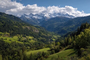 Fototapeta premium Mountain valley vista, snow capped peaks in the distance, green hills and forests below