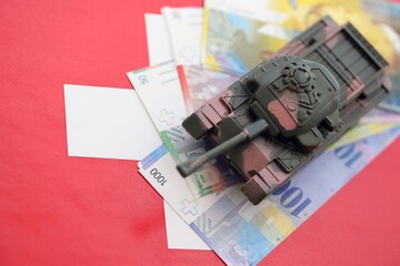 Swiss franc banknotes and toy tank on flag. The current francs money bills and tank lies on flag