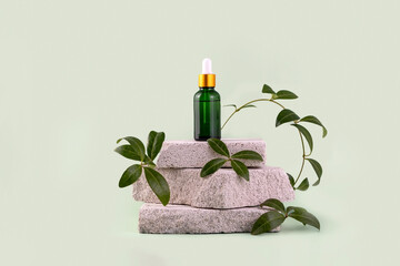 A bottle of fragrant oil on a stone podium. Essential oil or serum in a green bottle with a...