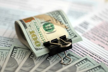 Big amount of United States hundred dollar bills in bunch on table with tax return form