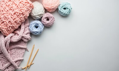 A cozy flat lay of pastel-colored yarn balls, knitting needles, and a half-finished scarf on a light gray surface.