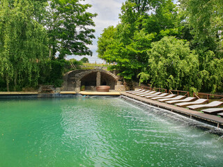 Summer outdoor swimming pool surrounded by fresh green grass and tall trees