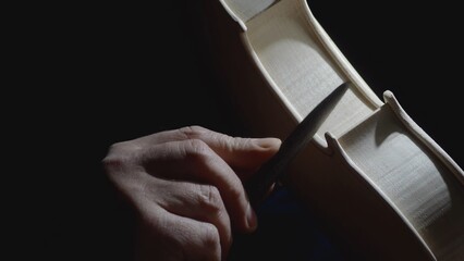 Skilled craftsman carefully filing intricate details of wooden violin body, highlighting meticulous...