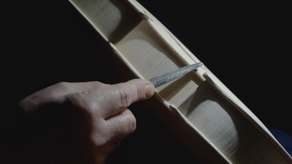 Skilled craftsman carefully filing intricate details of wooden violin body, highlighting meticulous...