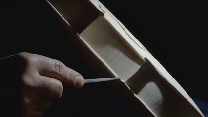 Skilled craftsman carefully filing intricate details of wooden violin body, highlighting meticulous...