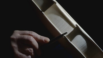 Skilled craftsman carefully filing intricate details of wooden violin body, highlighting meticulous...