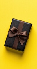 Black gift box with brown ribbon on yellow background