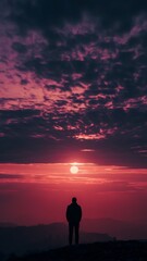 Fototapeta premium Silhouette of a person standing on a hilltop, gazing at a vibrant sunset sky.