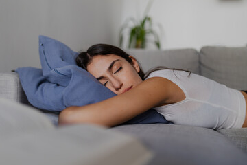 Serene moment of a young woman enjoying a peaceful nap on a comfortable sofa, embracing a blue...